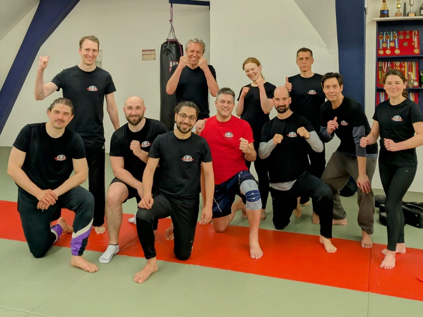 Grosse Trainingsgruppe von Krav Maga Zürich auf der Matte mit erhobenen Fäusten